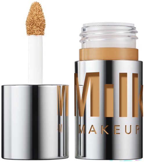 A liquid concealer stick with a sponge applicator and a shiny silver container with brown and gold text.