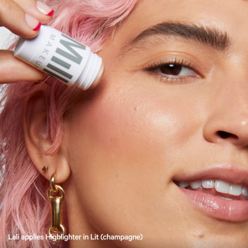 Een vrouw met roze haar brengt highlighter aan op haar gezicht.