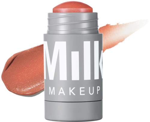 Een zilverkleurige tube met 'Milk Makeup' label, met een perzikkleurige balsem of lippenstift, en monsters van het product op een witte achtergrond.