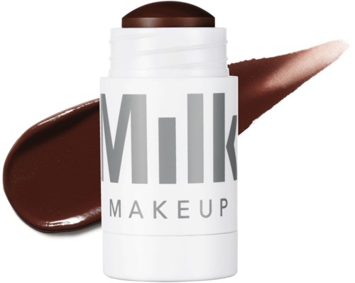 Een witte container met 'Milk Makeup' erop en een bruin deksel, met monsters van bruin lipstick of crème product erachter en ernaast.