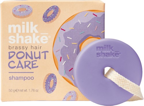 Een paarse donutvormige shampoo bar met touw, naast een doos met donutillustraties en paarse glazuur.