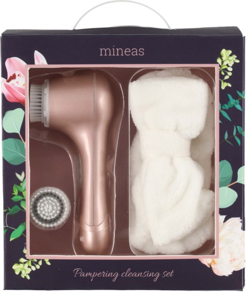 A skincare cleaning set with a pink facial cleansing device, a round brush, and soft white cloths in a floral box.