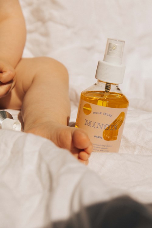 Babyhand neben einer kleinen Flasche mit gelber Flüssigkeit auf einem Bett.