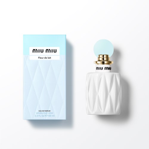 Een parfumfles met diamantpatroon en blauwe label naast een blauwe doos, beiden met 'Miu Miu Fleur de lait' geschreven.