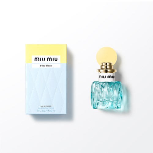 Een parfumfles en doos. De fles is lichtblauw met een ronde gele dop. De doos is blauw en geel met tekst.