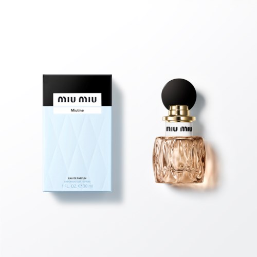 Miu Miu parfum genaamd Minutie in een glazen fles met een zwarte bolkap, naast de doos.