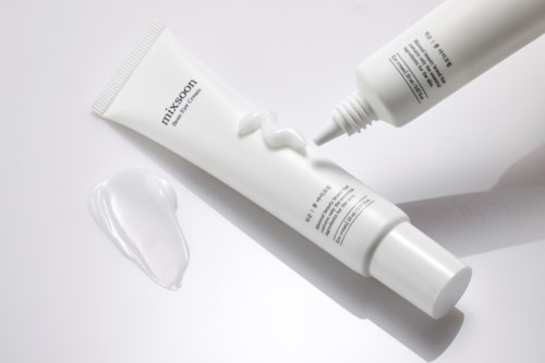 Twee witte tubes met crème, één knijpt crème uit op een oppervlak, op een witte achtergrond.