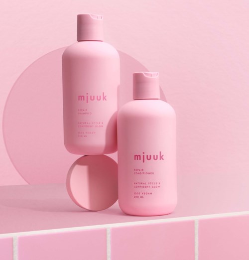 Zwei rosa Flaschen mit der Aufschrift 'mJUk' stehen auf einer rosa gefliesten Oberfläche, mit einem rosa Kreis im Hintergrund.