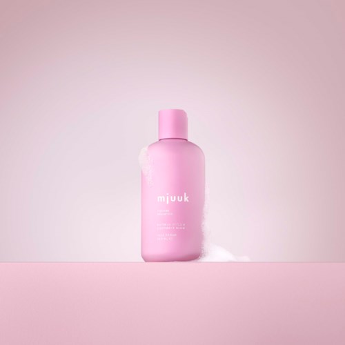 Een roze fles met een wit label op een roze oppervlakte, met een lichtroze achtergrond.