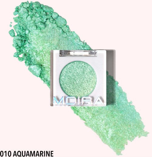 A square eyeshadow compact labeled 'Moira' with light green, shimmery eyeshadow spilled behind it.