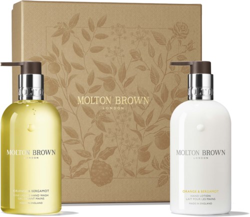 Zwei Flaschen Handwasch- und Handlotion mit einer beigen Schachtel und Blumenmuster dahinter.