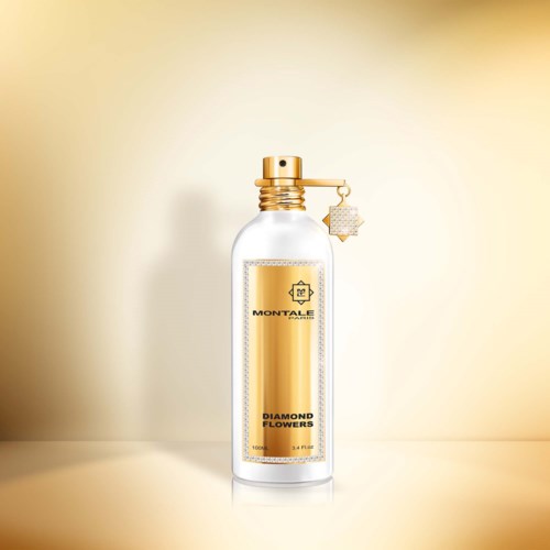 Een heldere parfumbottle met gouden accenten en een diamantbloemlabel, staat op een neutrale achtergrond.