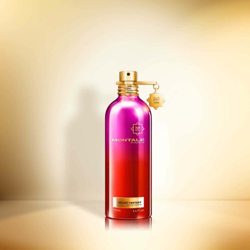 Een lange, glanzende, roze en gouden fles met dop en een kleine hangende tag. Het heeft een label dat zegt "Velvet Fantasy".