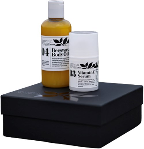 Twee flessen huidverzorgingsproducten op een zwart doosje. Labels vermelden Bijenwas Lichaamsolie en Vitamine C Serum.