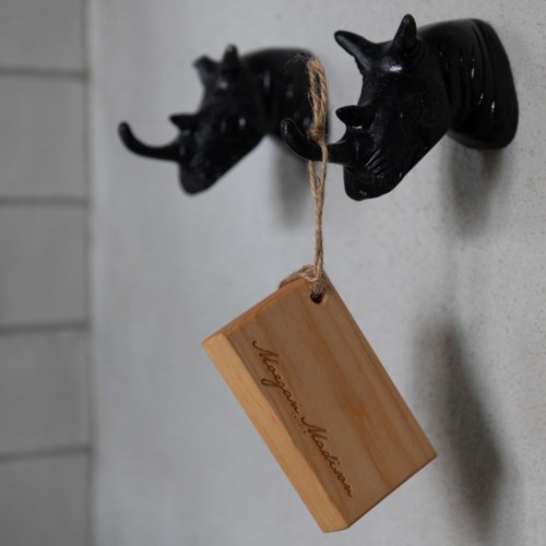 Two black animal head hooks hold a wooden tag with text on a light wall.