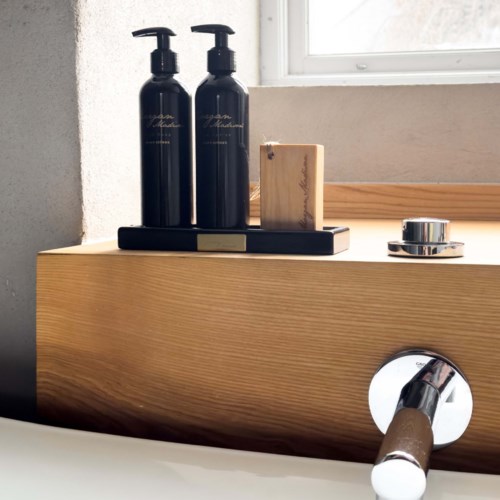 Two black bottles are on a wooden shelf next to a small wooden box and metal accessories, near a window.