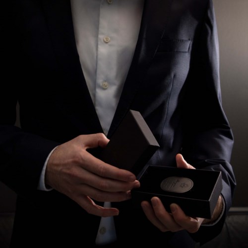 A person in a suit holds a box, possibly with a gift or product inside, in a dimly lit setting.