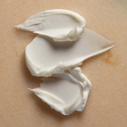 Tre lag med myk, hvit krem spredt på en brun overflate, sannsynligvis brød eller bakverk. Enkel og jevn tekstur.