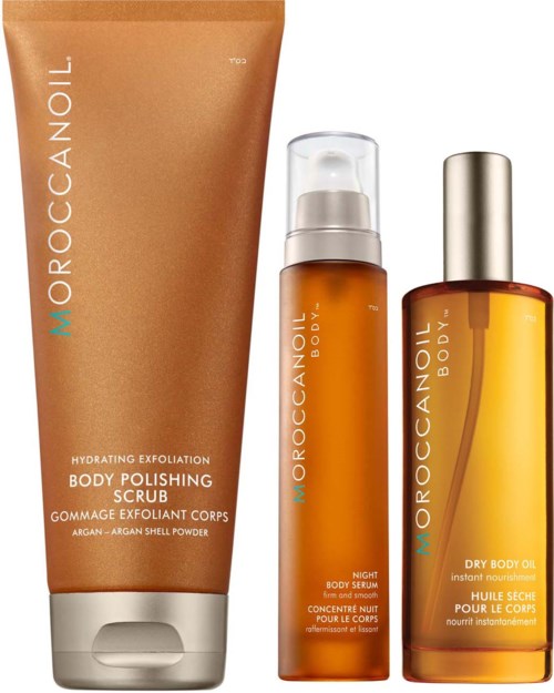 Three orange-colored skincare products: scrub, night serum, and dry body oil, with silver and white caps.