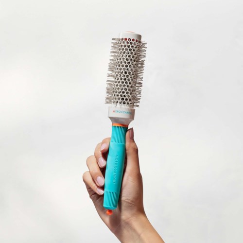 A hand holds a round hairbrush with bristles and a white and blue handle.