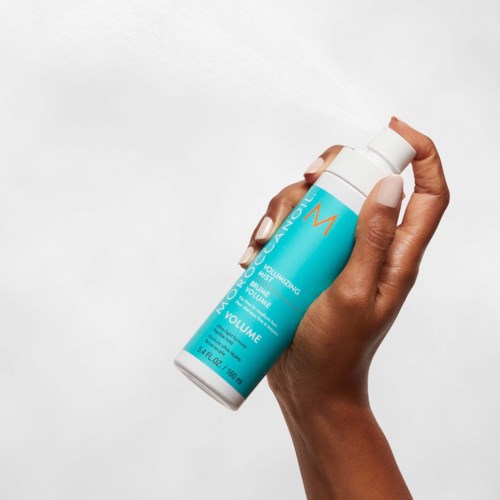 A hand holding a blue and white can of volumizing mousse. The can has text and a logo on it.