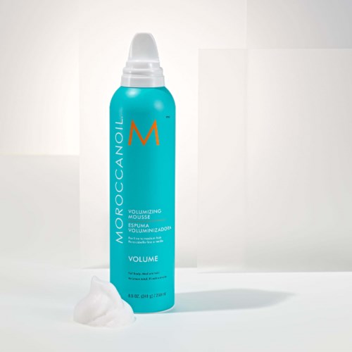 A blue bottle of Moroccanoil volumizing mousse with foam at its base.