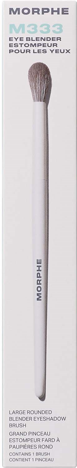 A long, white makeup brush with soft bristles and a rounded tip, in front of white packaging.