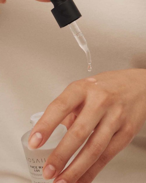 En hand håller en liten vit flaska med en droppe flytande som faller från en pipett.
