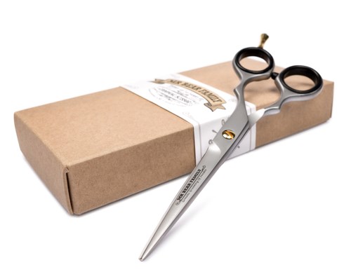 A pair of small scissors placed on a brown paper package with a white label. The scissors are silver with black handles.