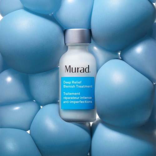 Een flesje met Murad Deep Relief Blemish Treatment tussen blauwe ballonnen.