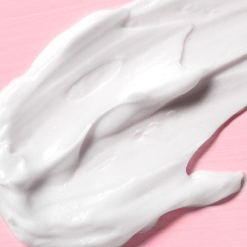 White cream spread on a pink surface, looks smooth and soft.