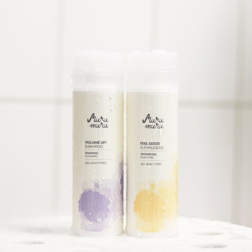 Two bottles of shampoo and shower gel stand side by side on a white surface, with water droplets on the bottles.