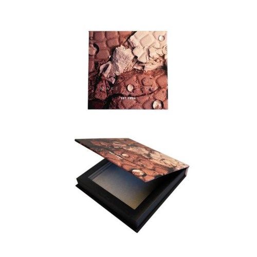En makeuppalett med olika puderskuggor och ett kvadratiskt lock med ett texturerat mönster. Paletten är öppen.