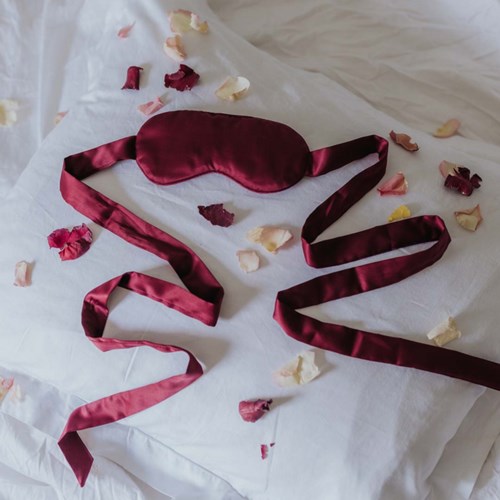 Eine rote Satin-Nackenkappe mit langen Bändern liegt auf weißem Laken, umgeben von bunten getrockneten Blütenblättern.