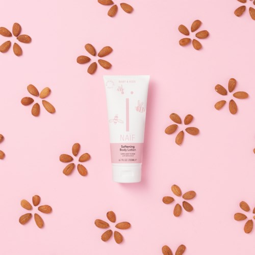 Eine weiße Tube mit Körperlotion, umgeben von verstreuten Mandeln auf rosa Hintergrund.