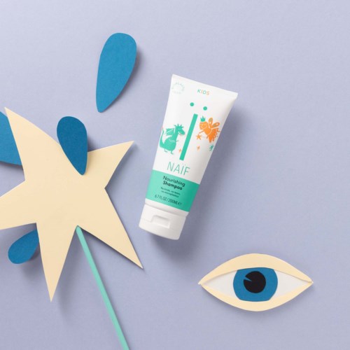 Eine Tube Shampoo, Papierausschnitte eines Sterns und eines Auges auf einem Pastellhintergrund.