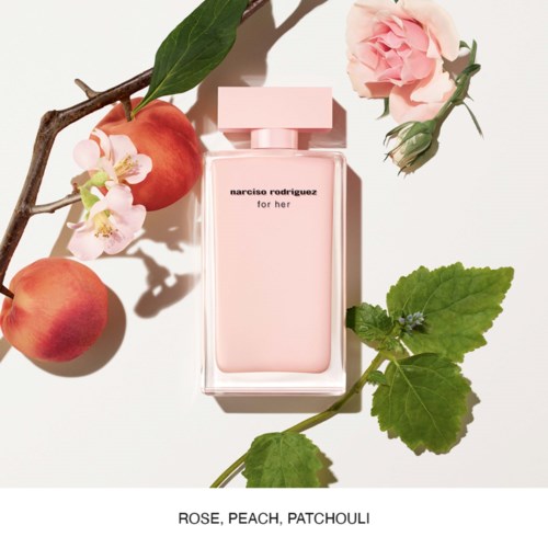 Een parfumfles met 'Narciso Rodriguez for her', omringd door roze rozen, perziken en groene bladeren.