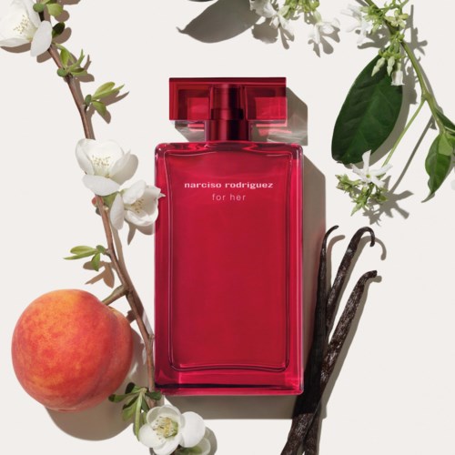 Een felroze parfumfles omringd door bloemen, een abrikoos en vanillebonen.