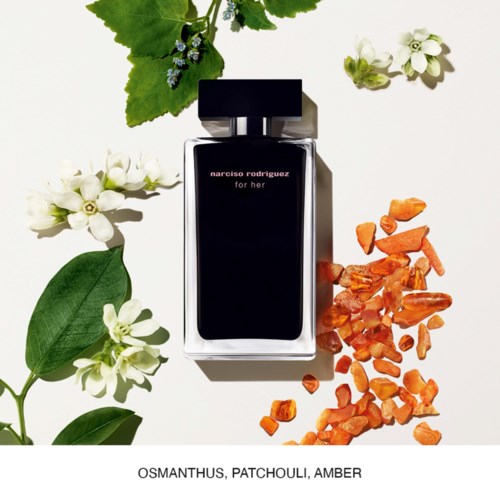 Een parfumfles met label 'narciso rodriguez for her' omgeven door groene bladeren, witte bloemen en oranje amberstenen.