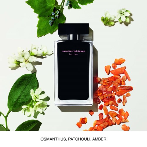 Een parfumfles omringd door groene bladeren, witte bloemen en oranje stenen, gemarkeerd 'narciso rodriguez for her.'