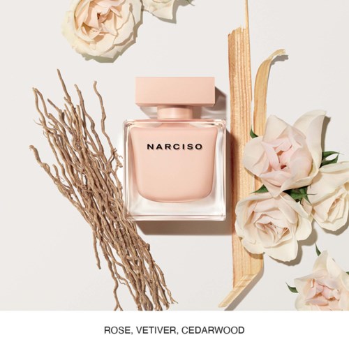 Een Narciso-parfumfles omgeven door lichte rozen, cederhout en vetiver op een schone achtergrond.