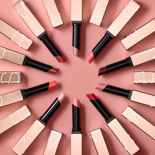 Läppstift arrangerade i en cirkel, med olika nyanser från nude till rött, på en rosa bakgrund.