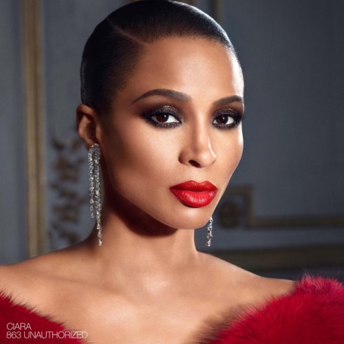 A woman with dark hair, wearing red lipstick, earrings, and a red fur garment, looking confidently at the camera.