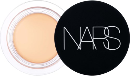 A compact cream container with an open lid, displaying a beige cosmetic product inside. The lid has the NARS logo.