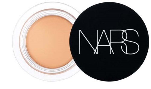 A round open container of beige makeup with a black lid displaying the NARS logo.