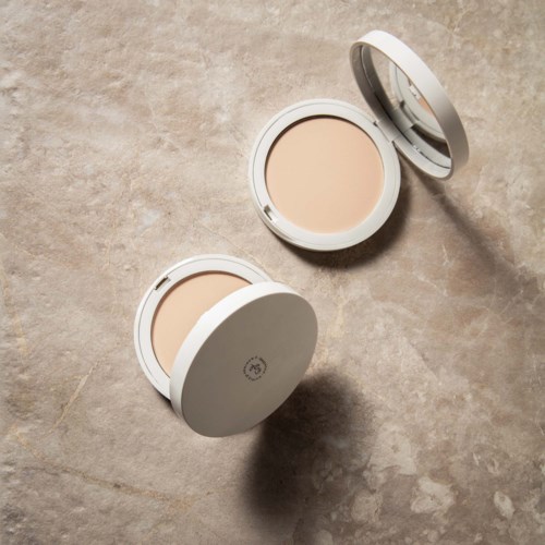 Twee ronde beige make-up poeders in witte containers op een grijze achtergrond. Eén deksel is open, laat het poeder zien.