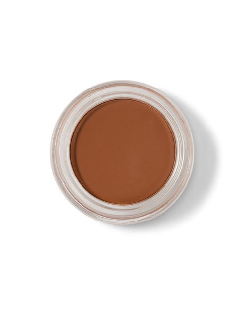 Een kleine ronde container met bruine make-up of crème erin, van boven op een witte achtergrond.