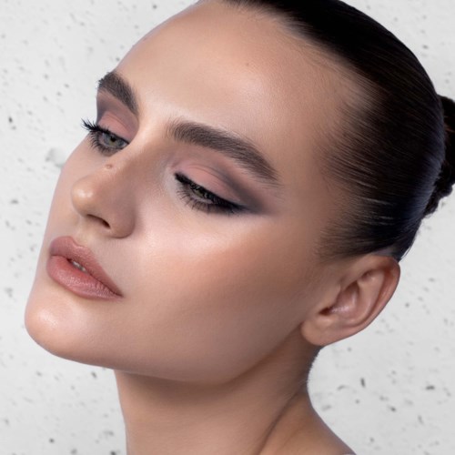 Eine Frau mit glatter Haut, dunklem Haar, das zurückgebunden ist, Make-up und ernstem Ausdruck.