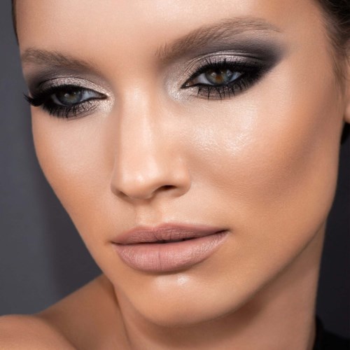 Nahaufnahme einer Frau mit dunklem Augen-Make-up, nude Lippen und glatter Haut.