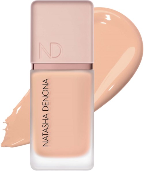 Eine beige Nagellackflasche mit rosa Deckel und dem Markennamen Natasha Denona. Etwas Nagellack ist dahinter verteilt.